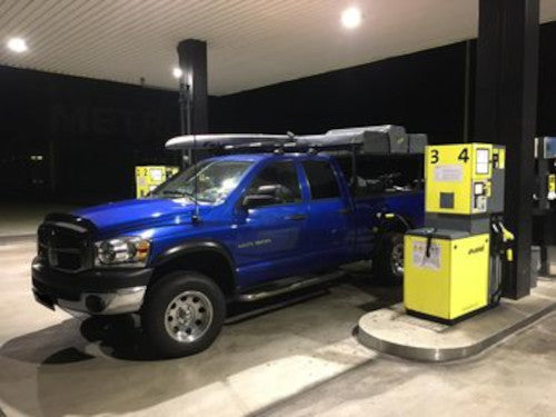 Pickup an einer Tankstelle mit Surfbrett auf dem Dach und Dachzelt auf der Ladefläche