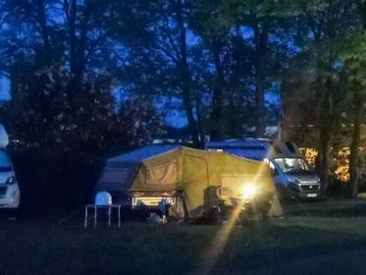 Anhängerzelt bei Abenddämmerung mit Spiegelung der untergehenden Sonne im Zeltfenster
