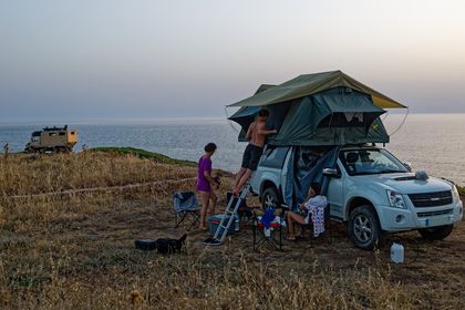 Familie vor und um das Auto mit zwei Dachzelten auf einer Klippe über dem Meer