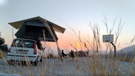 Kleinwagen mit Dachzelt auf Sandplatz mit Sonnenuntergang im Hintergrund