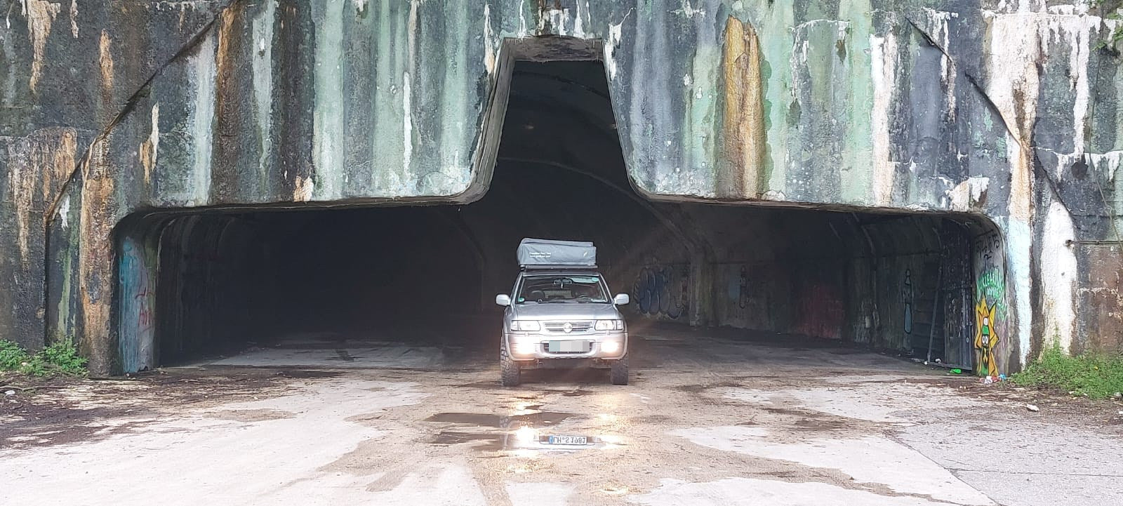 Auto mit Dachzelt fährt auf verlassenem Flugzeughangar in Kroatien