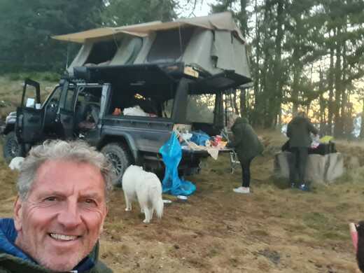 Selfi eines Mannes und im Hintergrund seine Familie und das Auto mit den zwei Dachzelten