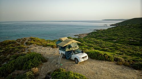 Zwei Dachzelte auf einem weißen Pickup auf Dünen mit Blick aufs Meer
