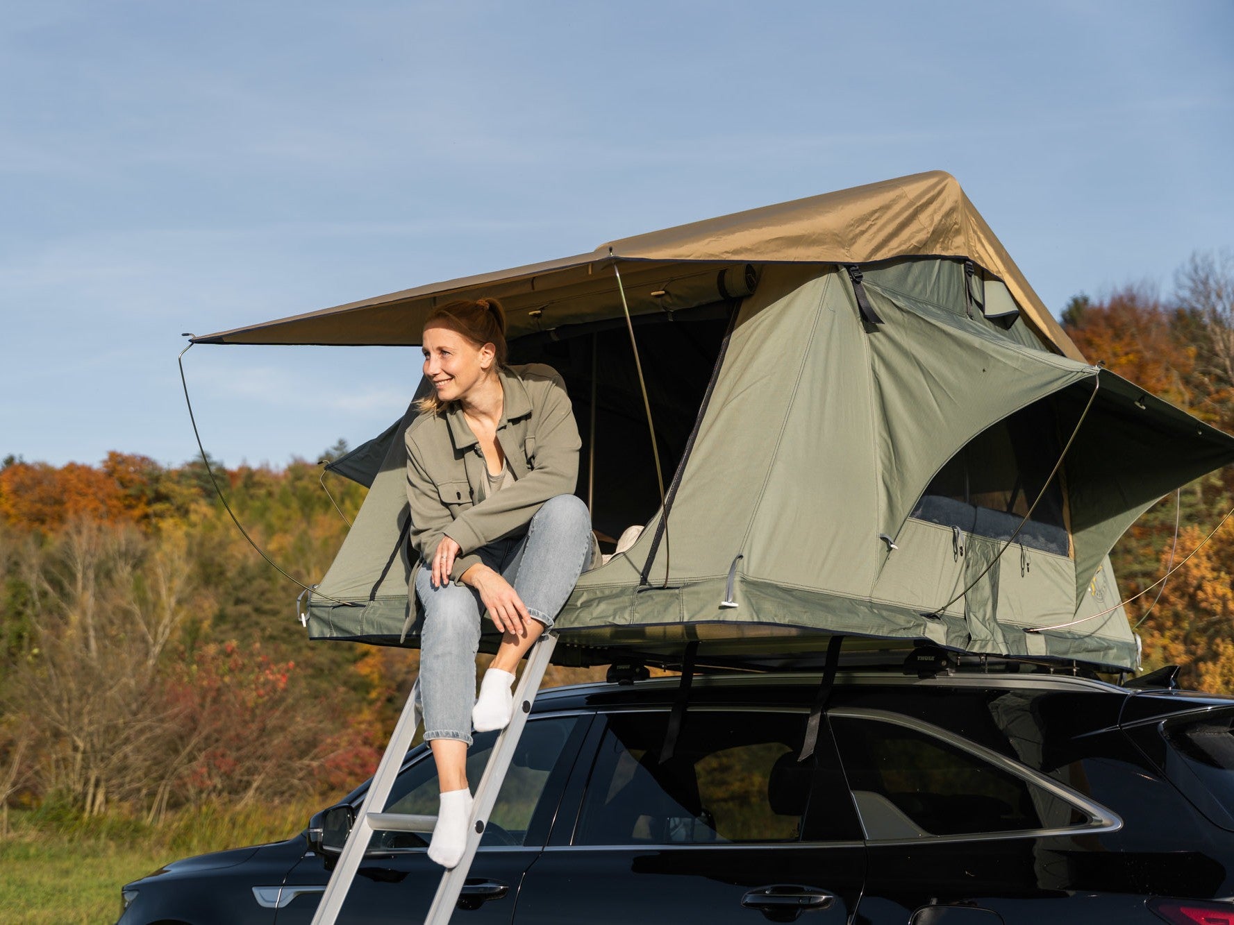 Dachzelt auf Auto, Frau sitzt im Eingang und lächelt