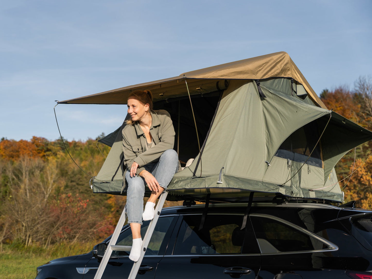 Dachzelt auf Auto, Frau sitzt im Eingang und lächelt