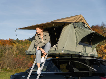 Dachzelt auf Auto, Frau sitzt im Eingang und lächelt