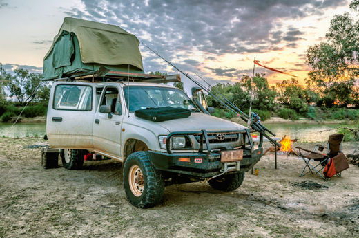 Toyota Hilux mit Dachzelt. Daneben Campingstuhl und Lagerfeuer